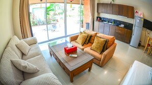 A living room with a sofa, a coffee table, and a kitchen area with cabinets and a refrigerator. - Tamnak Villa (Pattaya)