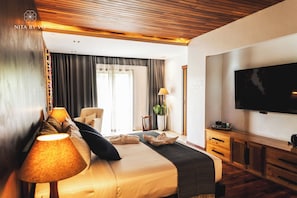 Una habitación de hotel con cama, televisión, escritorio y un amplio ventanal con cortinas.