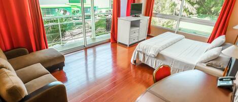 A hotel room with a bed, a desk with a TV, a sofa, and a view of the outside.