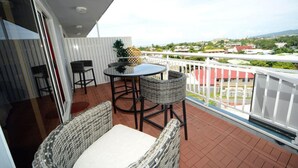 A balcony with wicker furniture, a table, and a view of a cityscape. - Hotel Sarah Nui (Papeete)