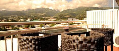 A balcony with wicker chairs and a table, overlooking a mountainous landscape.