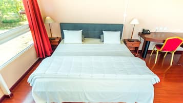 A hotel room with a large bed, a desk, a chair, and a window with curtains.
