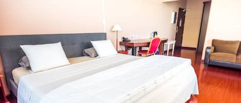 A hotel room with a large bed, a desk, a chair, and a small table.