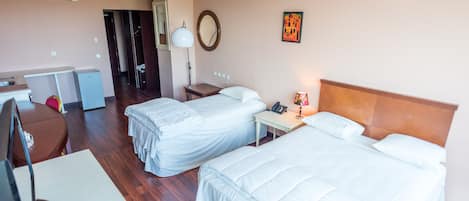 A hotel room with two beds, a desk with a computer, a TV, and a small kitchenette.
