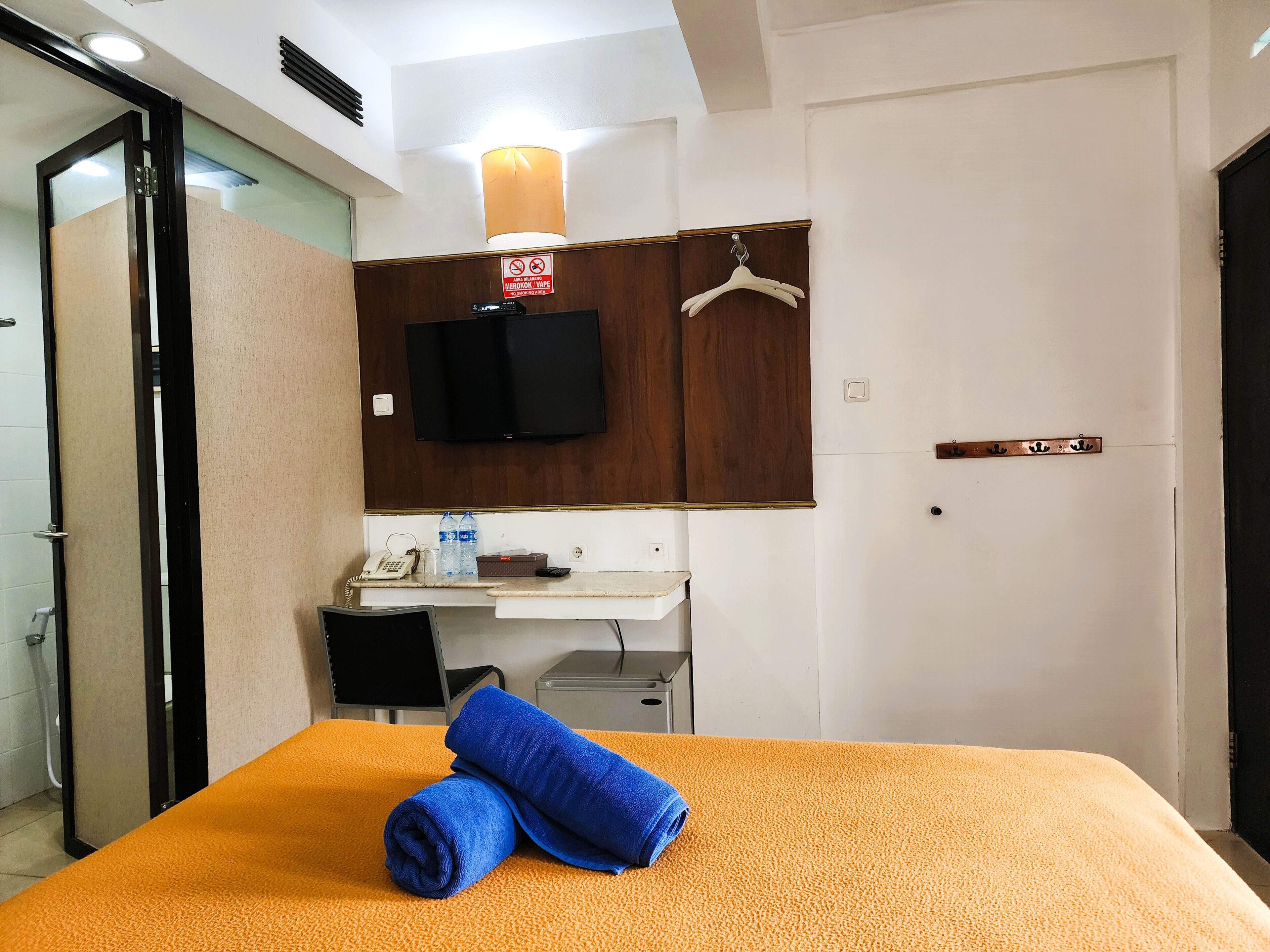 A hotel room with a bed, a desk, a television, and a sign prohibiting smoking.