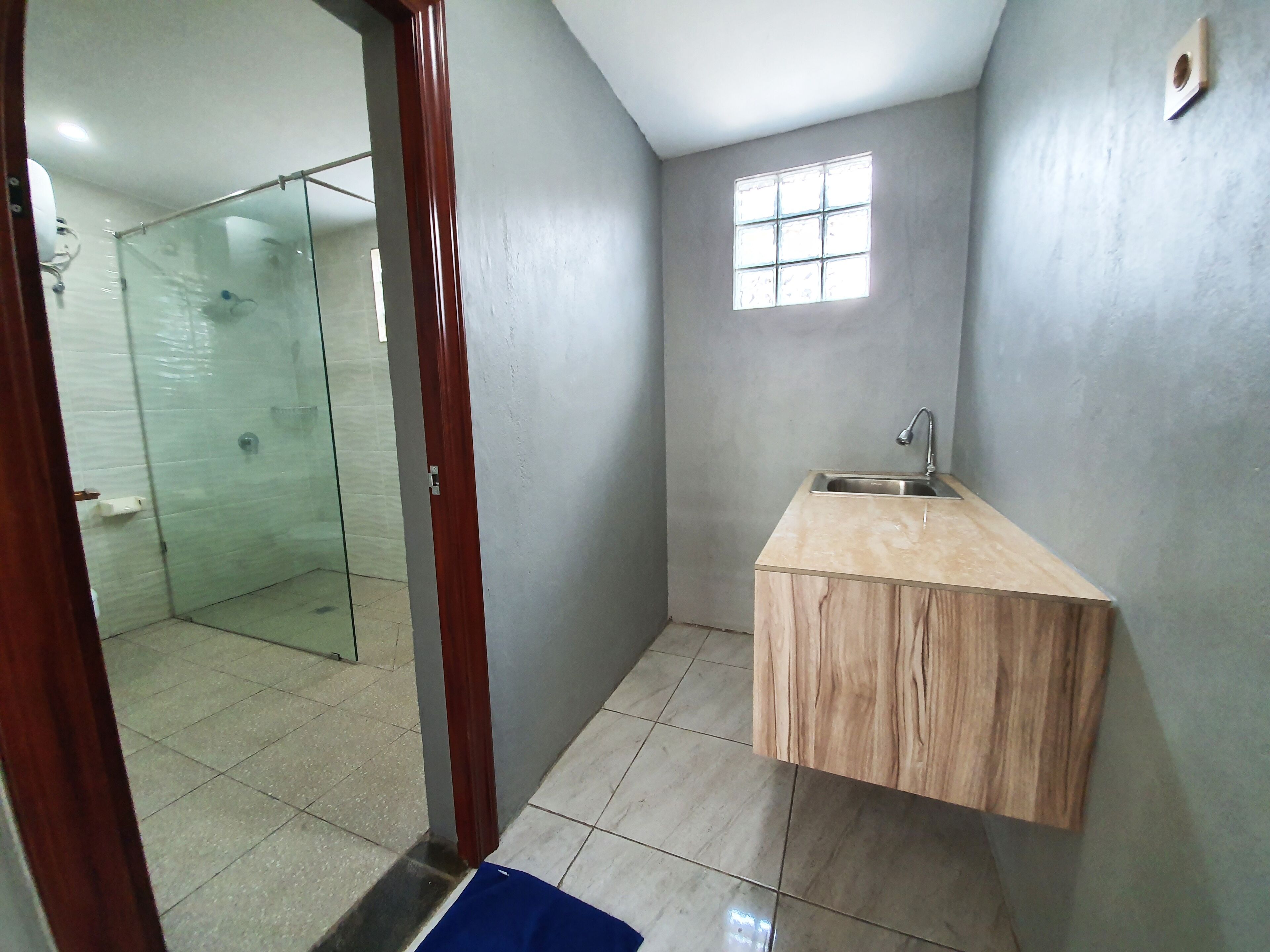 A bathroom with a glass shower enclosure, a wooden vanity with a sink, and a small window.