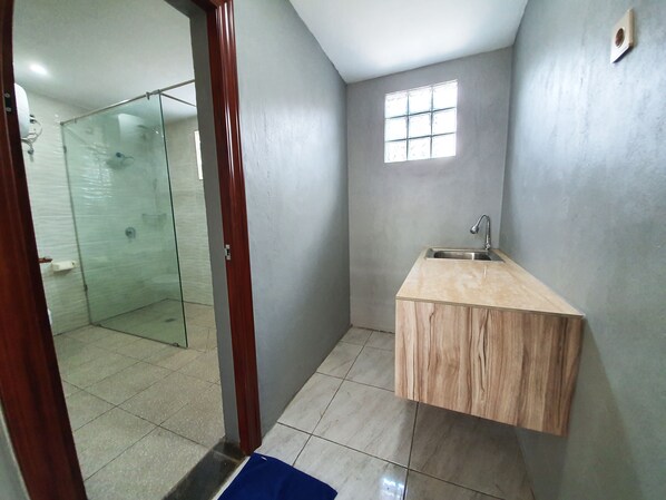 Un baño con cabina de ducha de vidrio, tocador de madera con lavamanos y un ventanal pequeño.