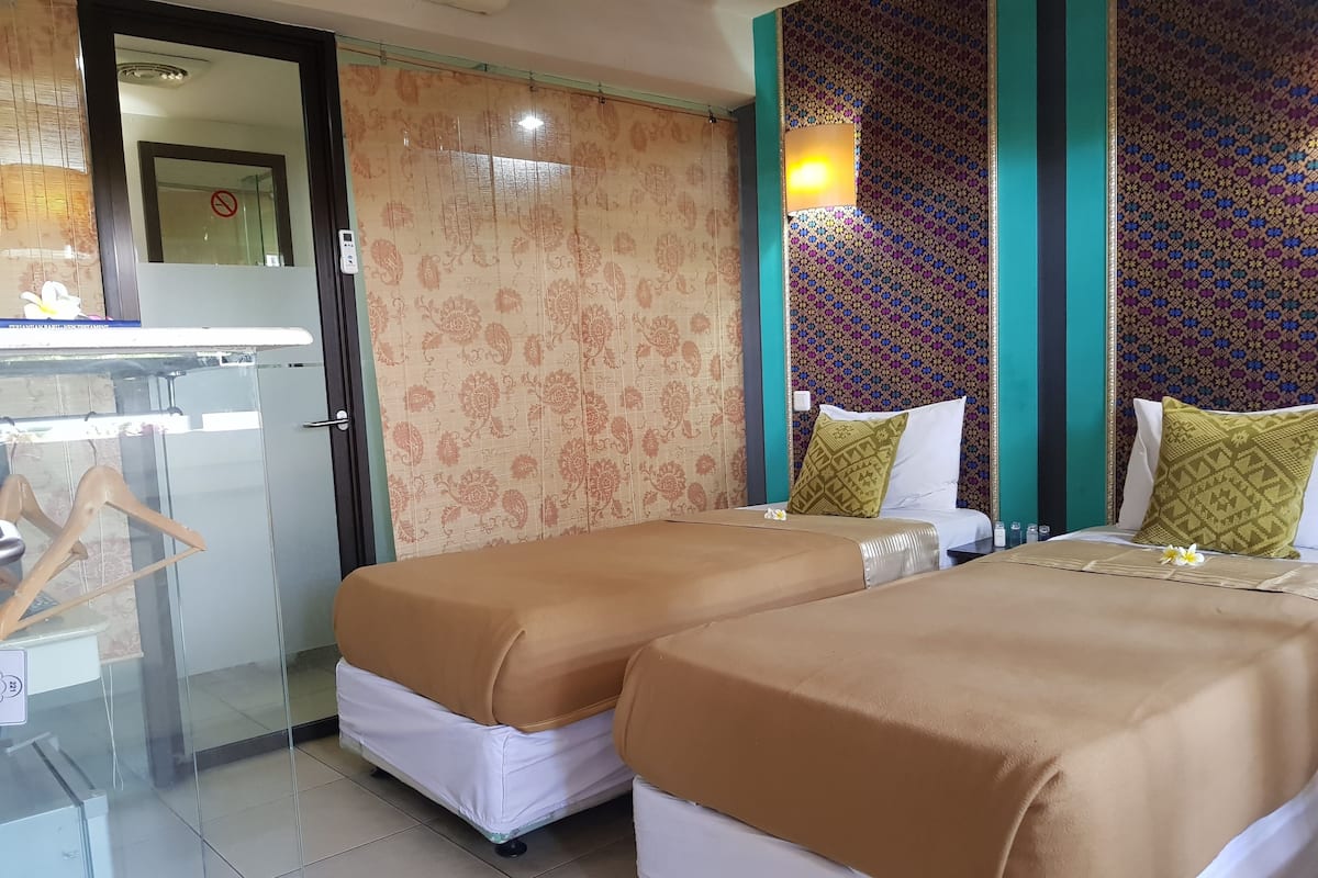 A hotel room with two beds, a glass partition, a wardrobe, and patterned wallpaper.