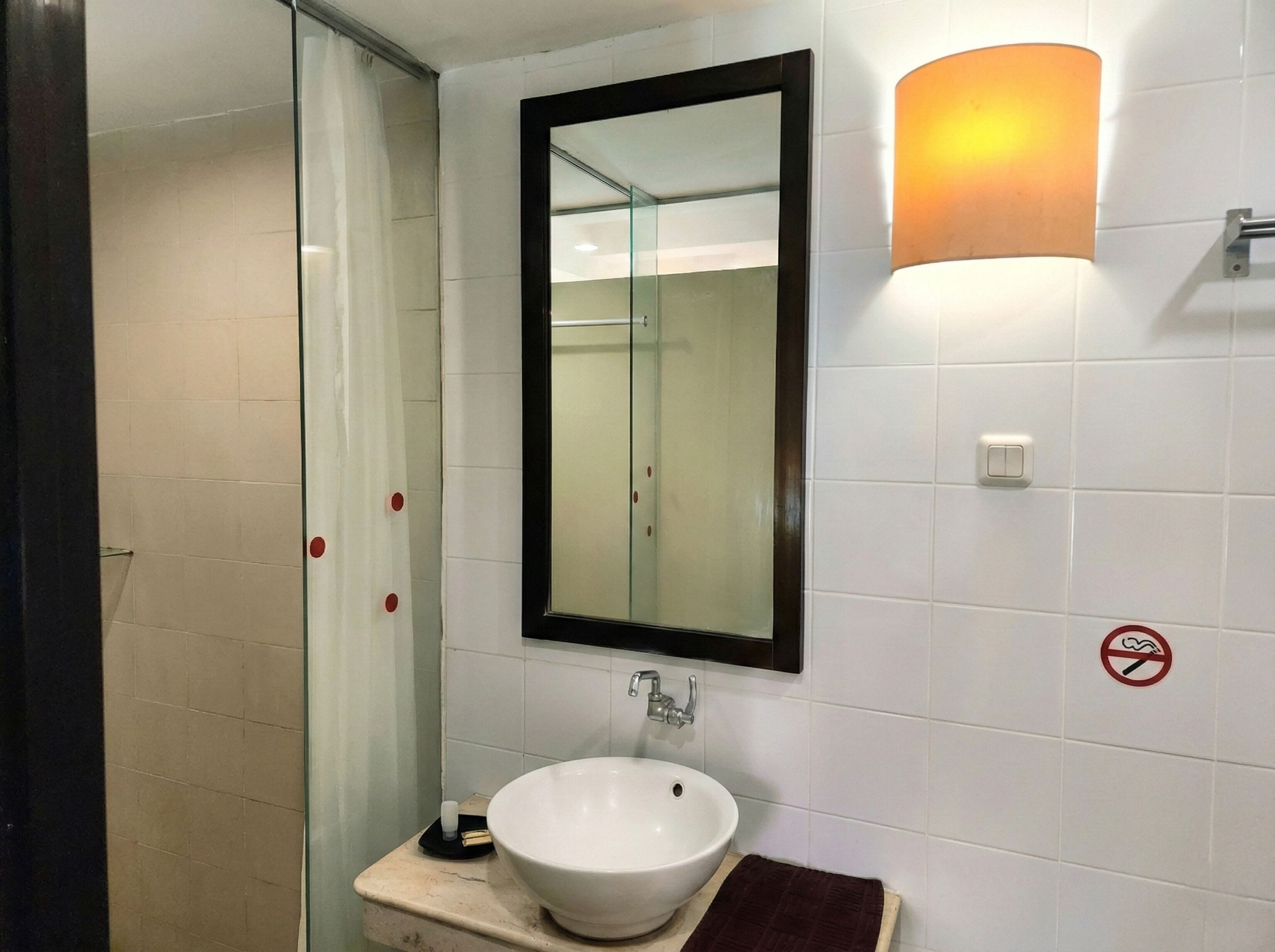 A bathroom with a white sink, a glass shower enclosure, a mirror, and a wall-mounted light fixture.