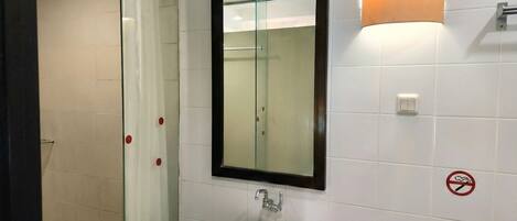 A bathroom with a white sink, a glass shower enclosure, a mirror, and a wall-mounted light fixture.