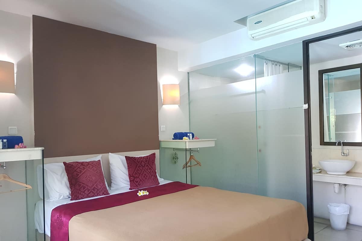 A hotel room with a bed, a bedside table, a mirror, a glass-enclosed shower, and a sink.
