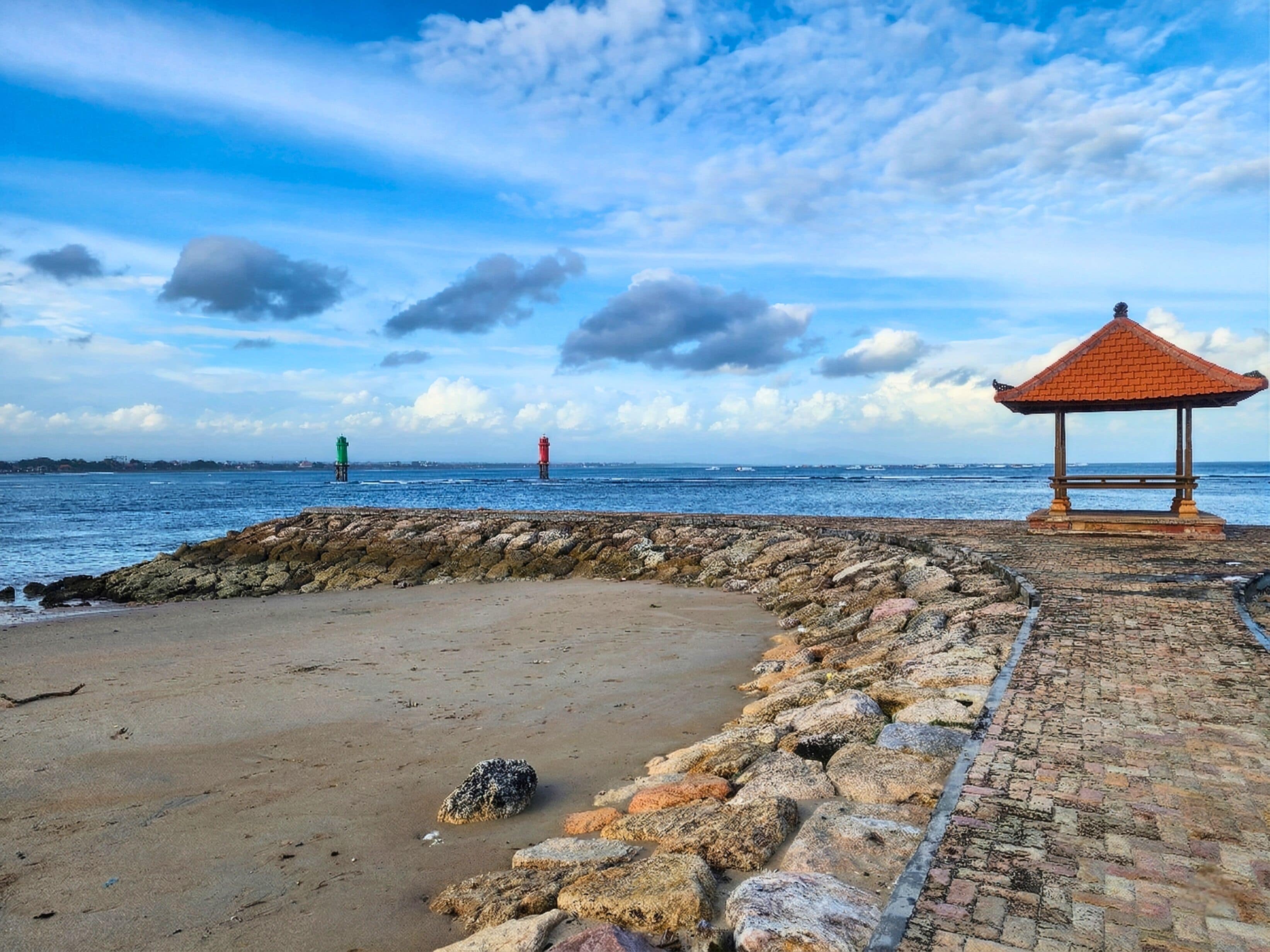 A coastal walkway with a gazebo and two lighthouses in the distance.