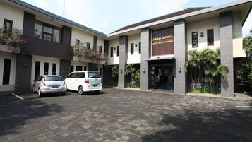 Un edificio moderno con un letrero que dice "SANUR AGUNG HOTEL & RESTAURANT". Dos coches estacionados en la parte delantera.
