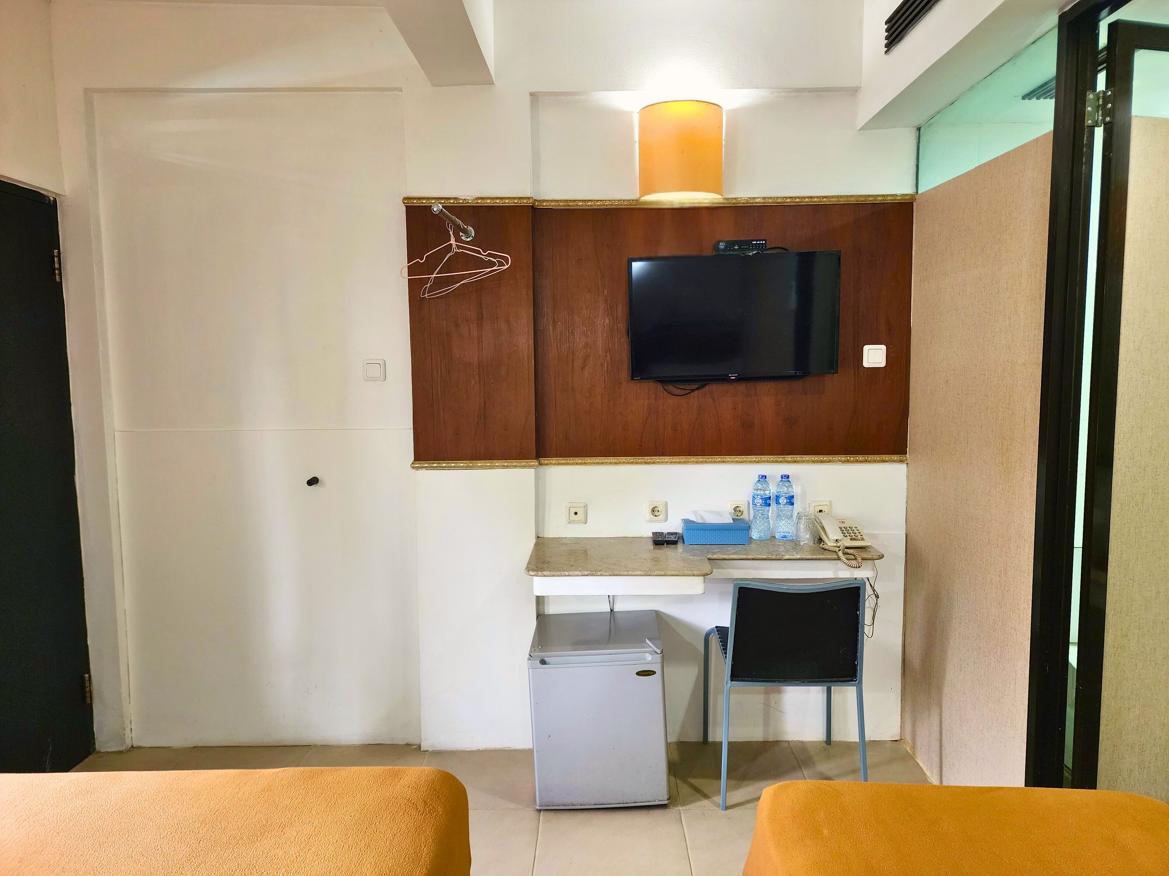 A compact hotel room with a kitchenette, a television, a small refrigerator, a desk with a chair, and two beds.