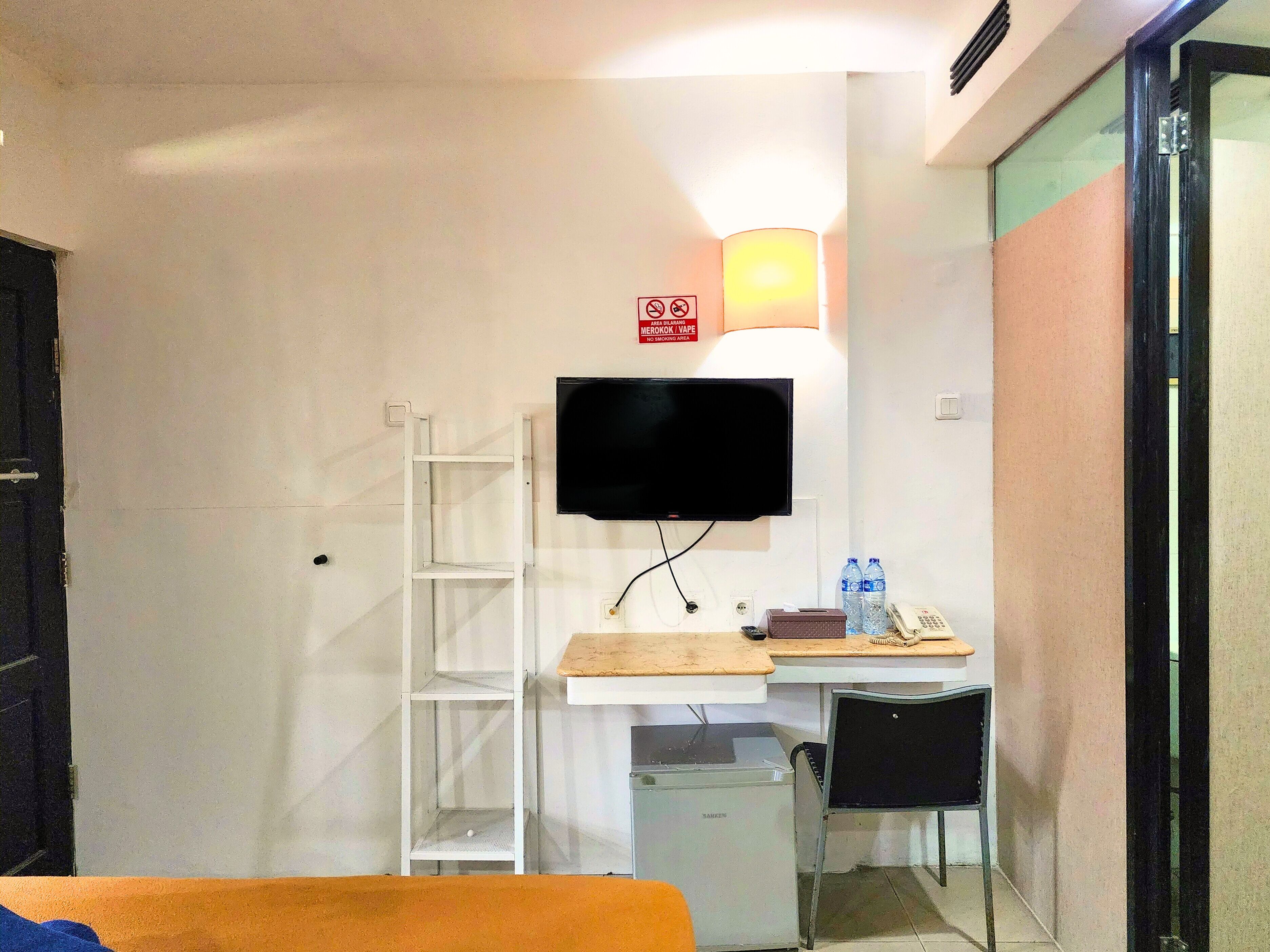 A hotel room with a bed, a desk with a chair, a TV mounted on the wall, a small heater, and a water bottle on the desk.