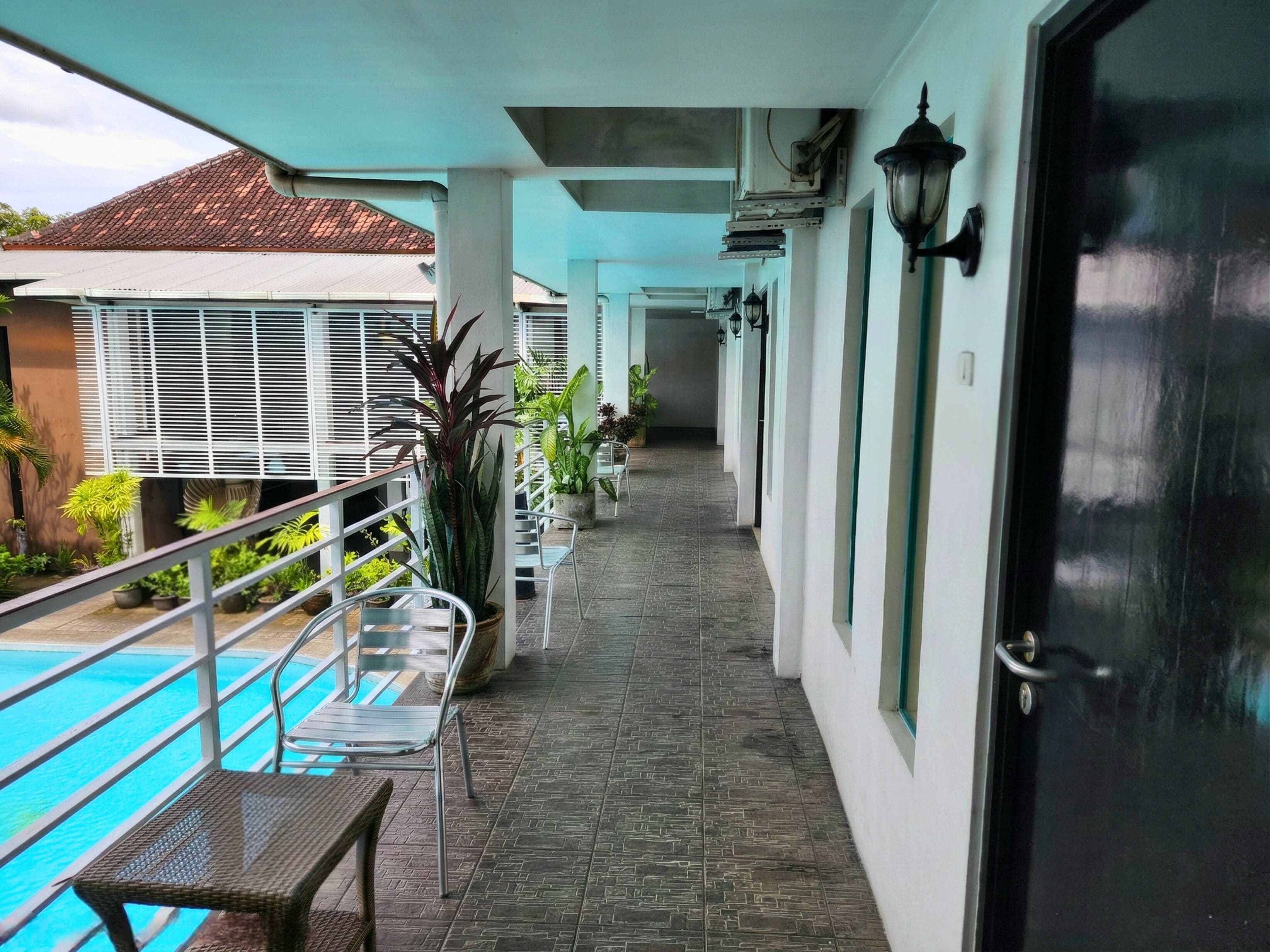 A covered outdoor area with a pool, chairs, potted plants, and a door.