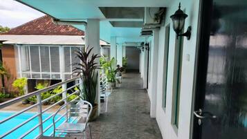 Un espacio exterior techado con piscina, sillas, plantas en macetas y una puerta.