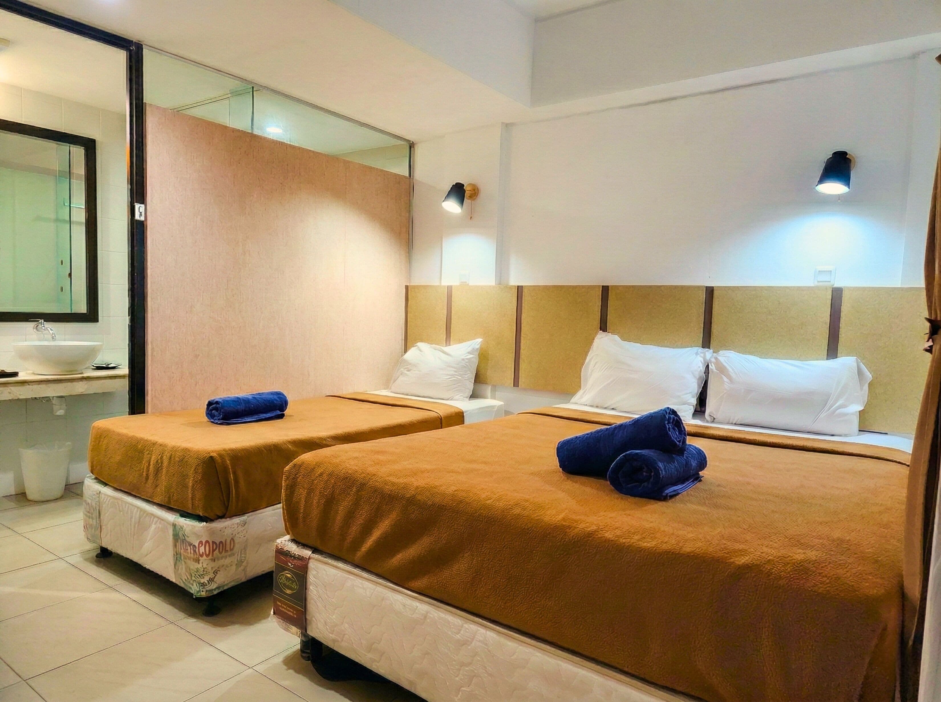 Habitación de hotel con dos camas, un baño con lavamanos y un espejo.