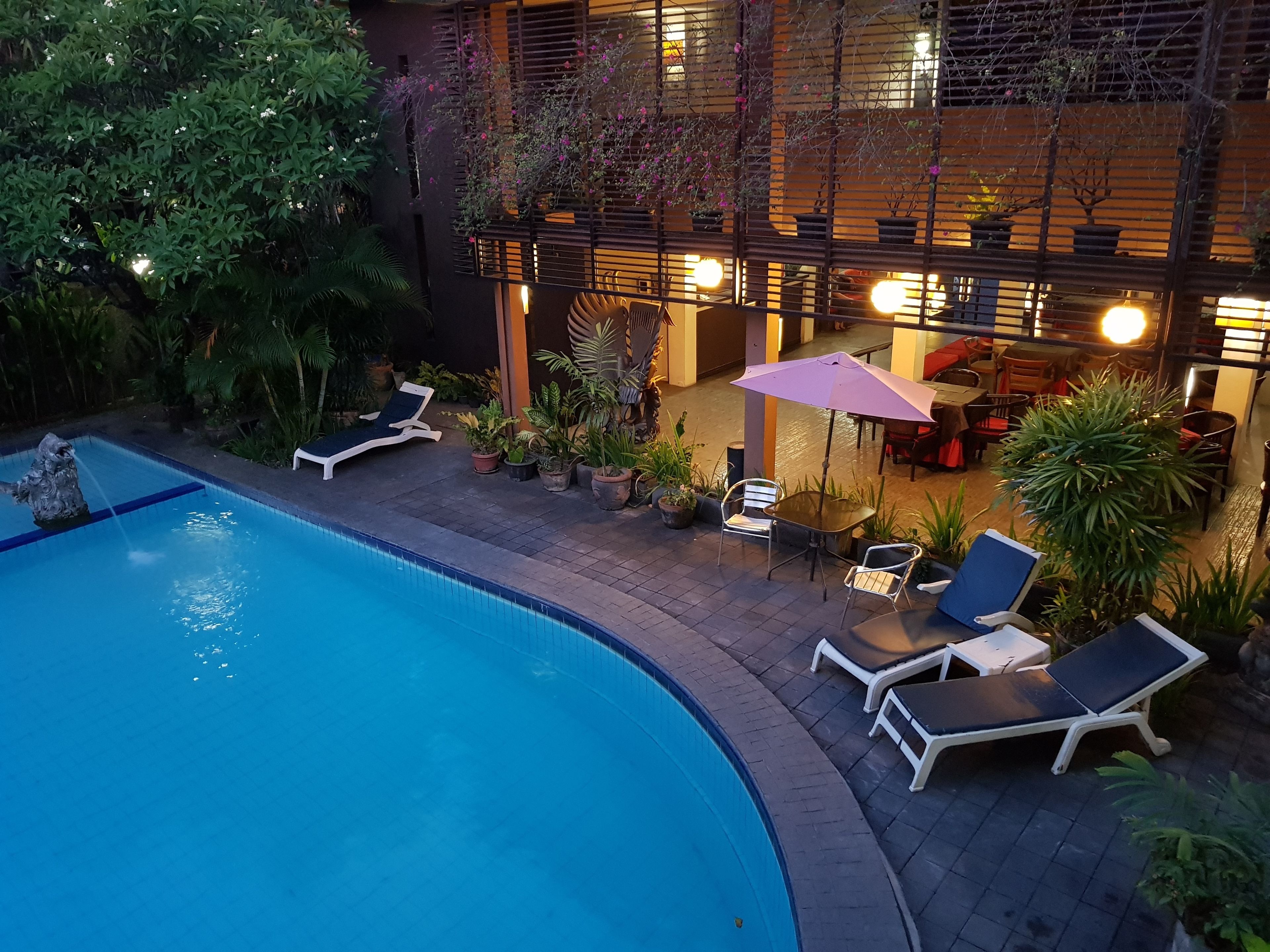 Zona de piscina exterior con sillones de descanso y una mesa con sombrilla.