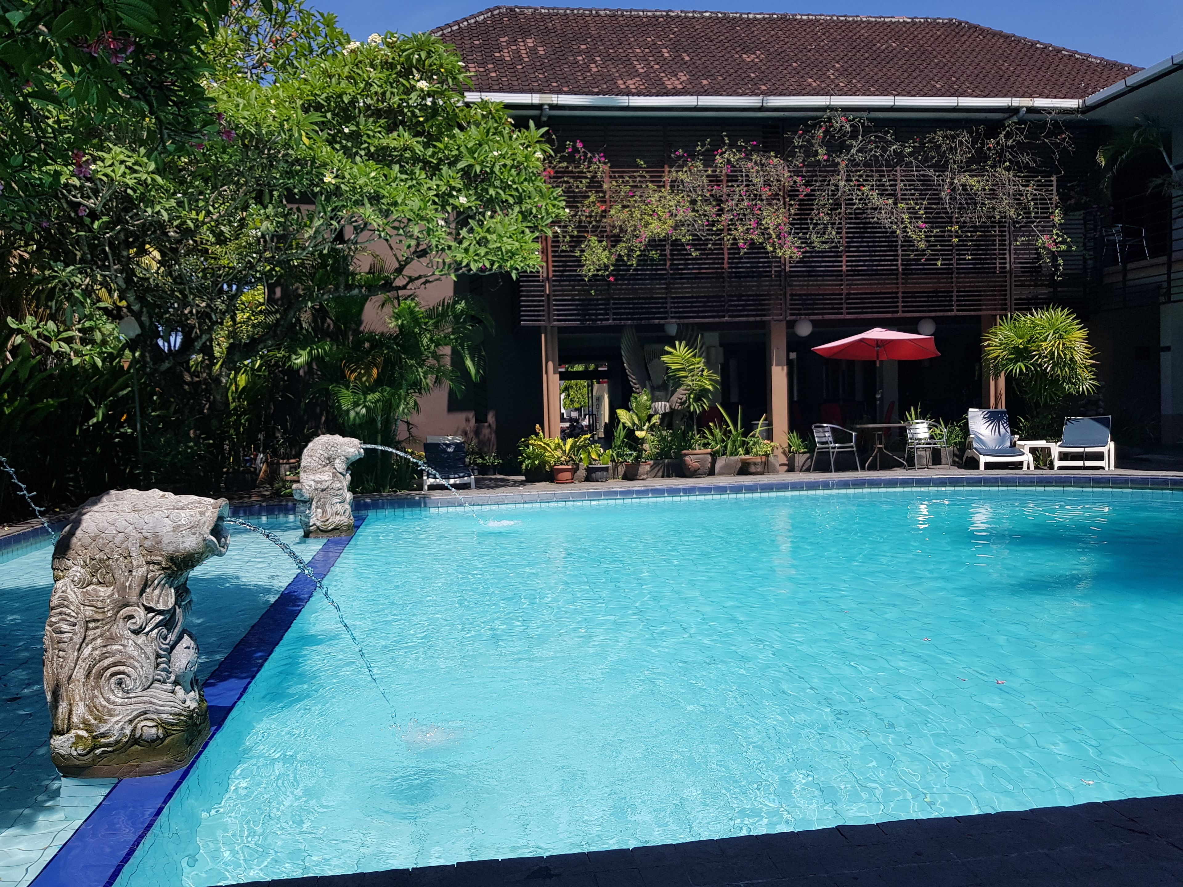 A swimming pool with a stone sculpture, surrounded by potted plants and outdoor seating.