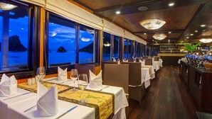 A restaurant with tables set for dining, large windows with a view of the sea, and a bar area with bottles and glasses. - Syrena Cruises (Tuan Chau)