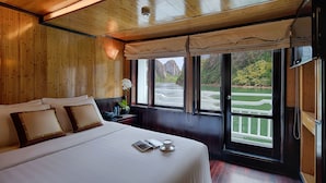 A hotel room with a large bed, a window with a view of a golf course, and wooden paneling. - Syrena Cruises (Tuan Chau)