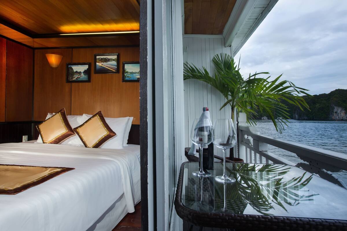 A bedroom with a bed, pillows, a nightstand, and a window overlooking a body of water.