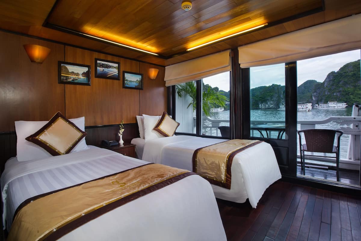 A hotel room with two beds, a large window with a view of the water and mountains, and wooden paneling.