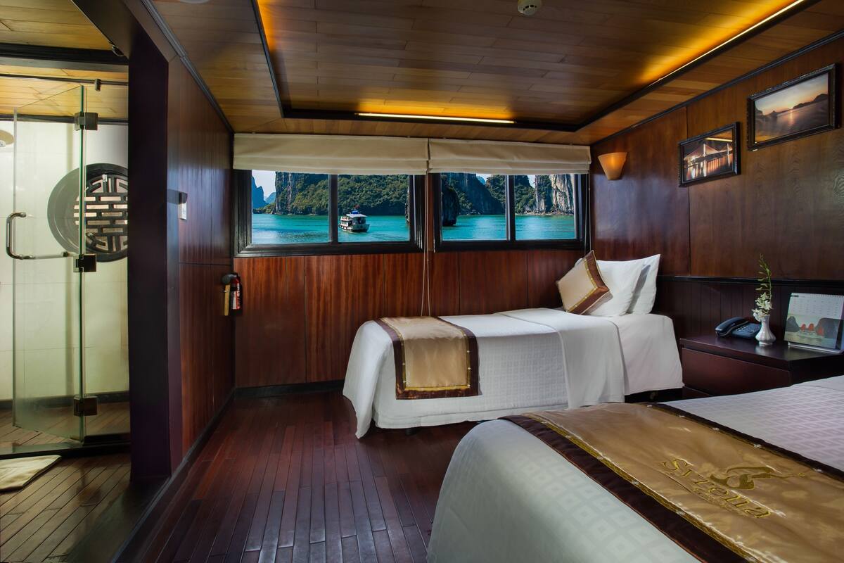A room with a bed, a desk, and a window with a view of a boat and water.