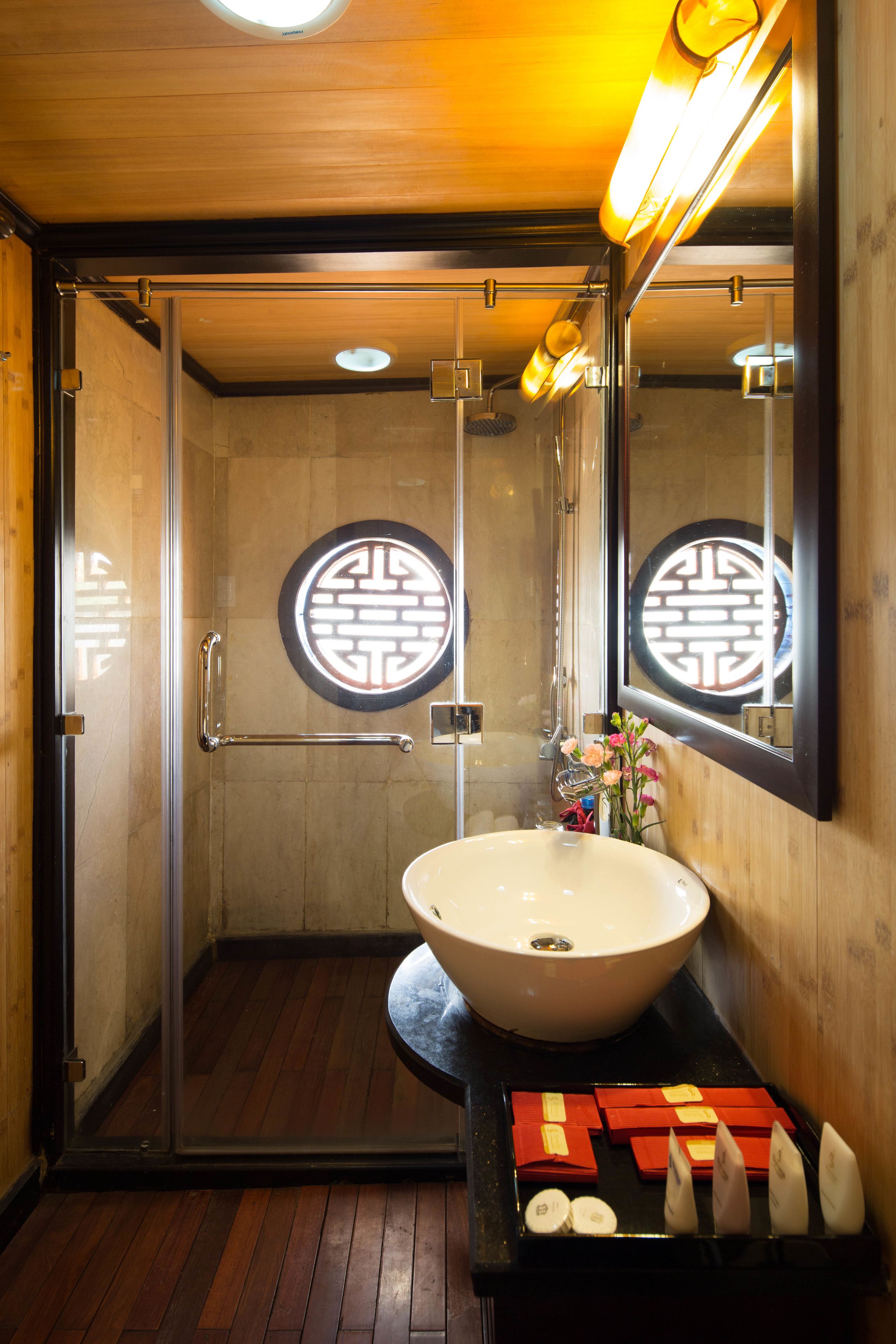 A modern bathroom with a glass-enclosed shower, a large sink, and a mirror reflecting a circular design on the wall.