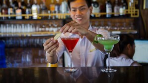 A bartender preparing drinks at a bar with shelves of bottles in the background. - Syrena Cruises (Tuan Chau)