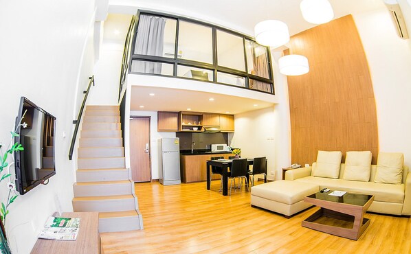 Un apartamento moderno con una escalera que sube a un dormitorio tipo loft, una zona de comedor y una sala de estar con sofá y mesa de centro.
