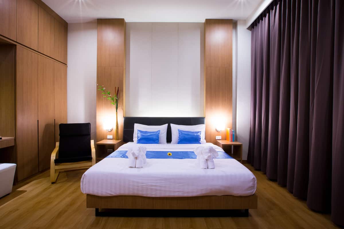A hotel room with a large bed, wooden wardrobe, and a nightstand with a lamp.