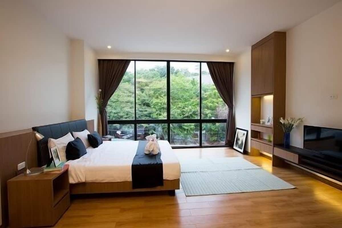 A modern bedroom with a large bed, a TV, and a view of greenery outside.