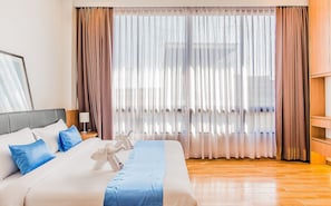 A hotel room with a large bed, a wooden floor, and a view through sheer curtains. - Sriracha Orchid (Si Racha)