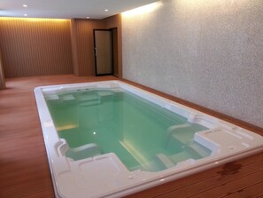 Una bañera de hidromasaje rectangular con superficie de agua cristalina, rodeada de suelo y paredes de madera con un diseño texturizado.