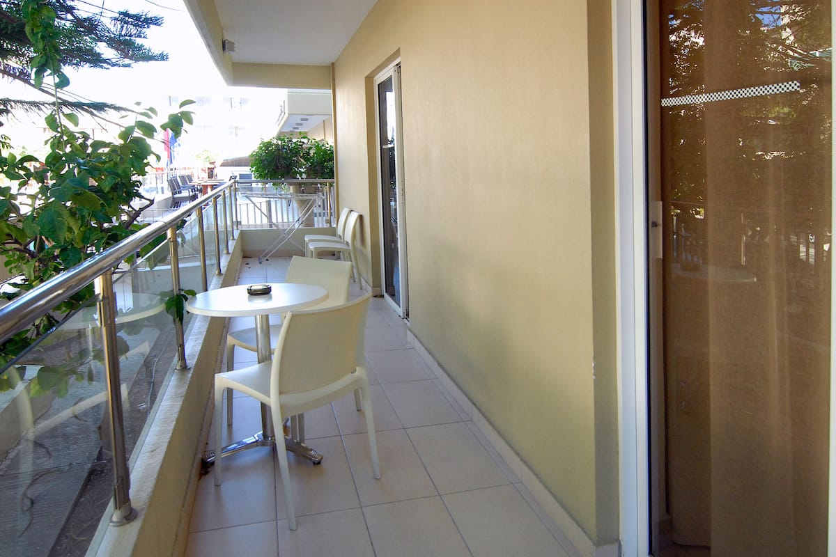 A balcony with a white table and chairs, a glass railing, and a view of the street.