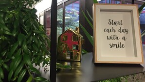 A framed inspirational quote on a shelf, a small golden house model, and a potted plant. - L'Acanthe Hôtel (Erbree)