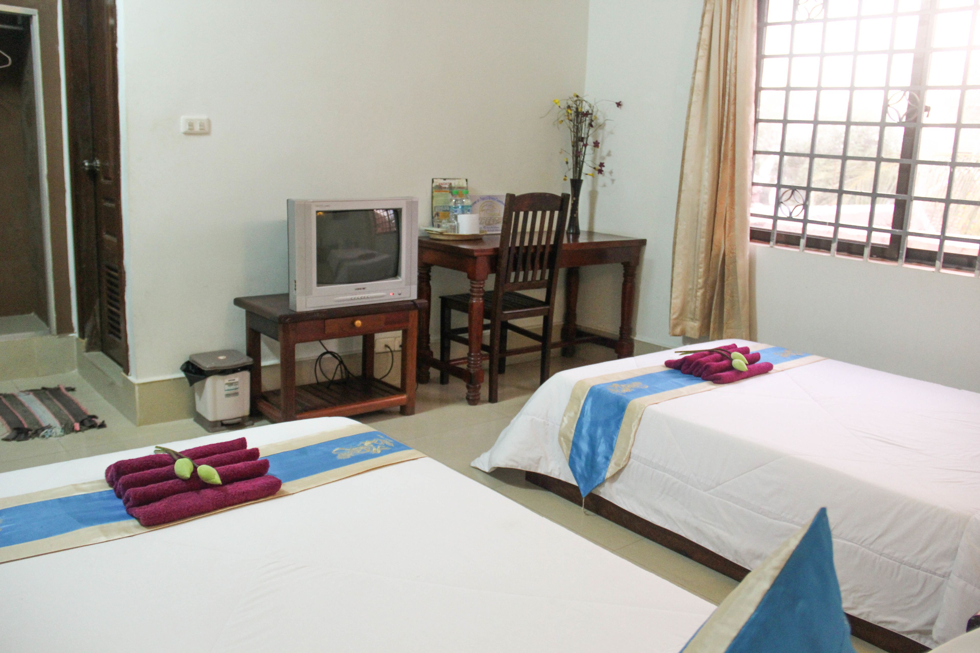 Habitación de hotel con dos camas, televisión, escritorio y ventana con cortinas.