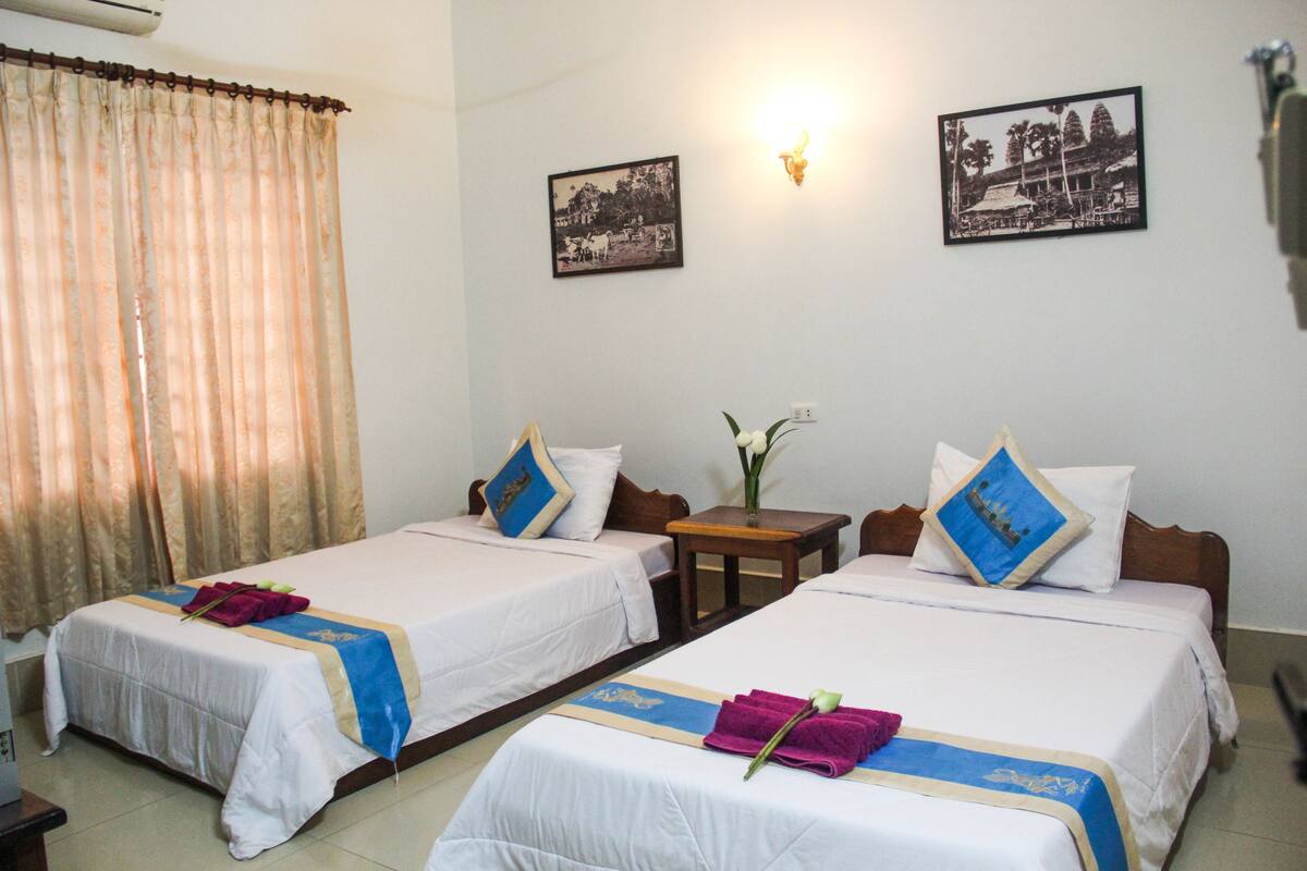 A hotel room with two single beds, each with a blue and white bedspread, and a wooden nightstand between them.