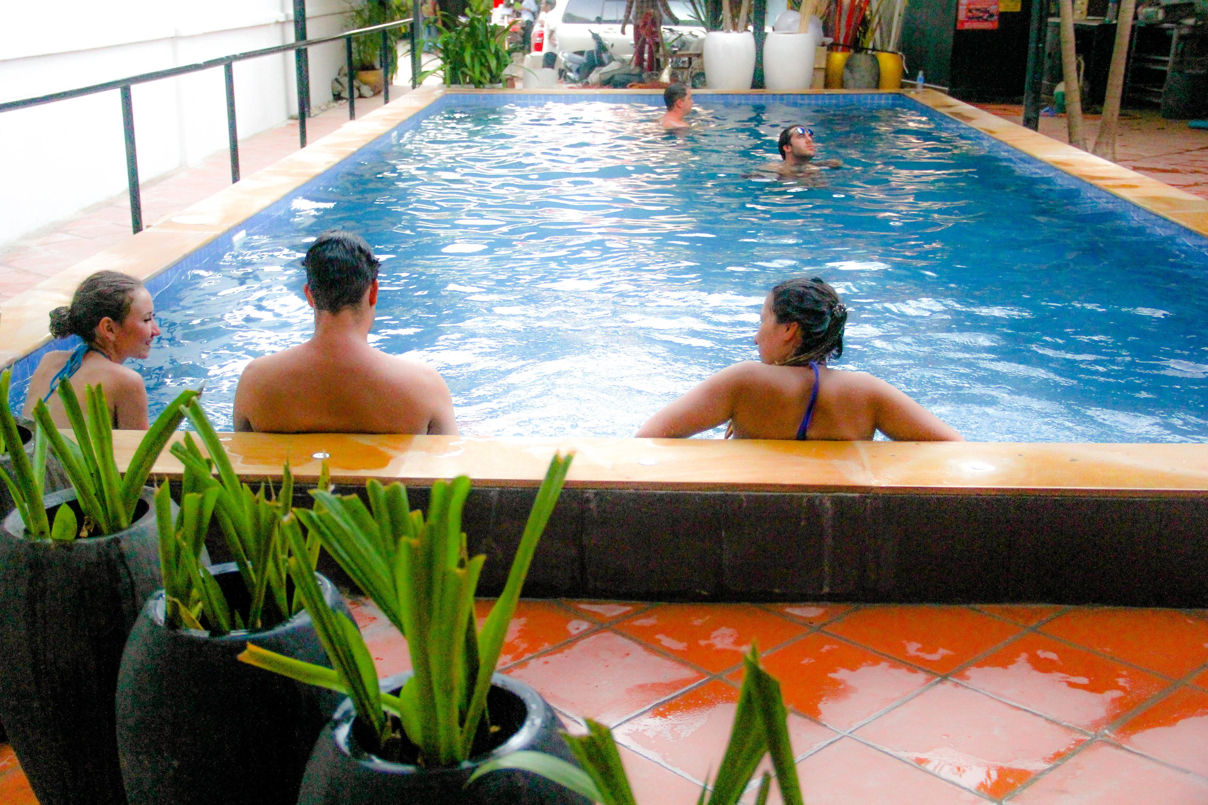 Une piscine où l’on voit des personnes dans l’eau, entourée de plantes en pot et dotée d’un sol carrelé.