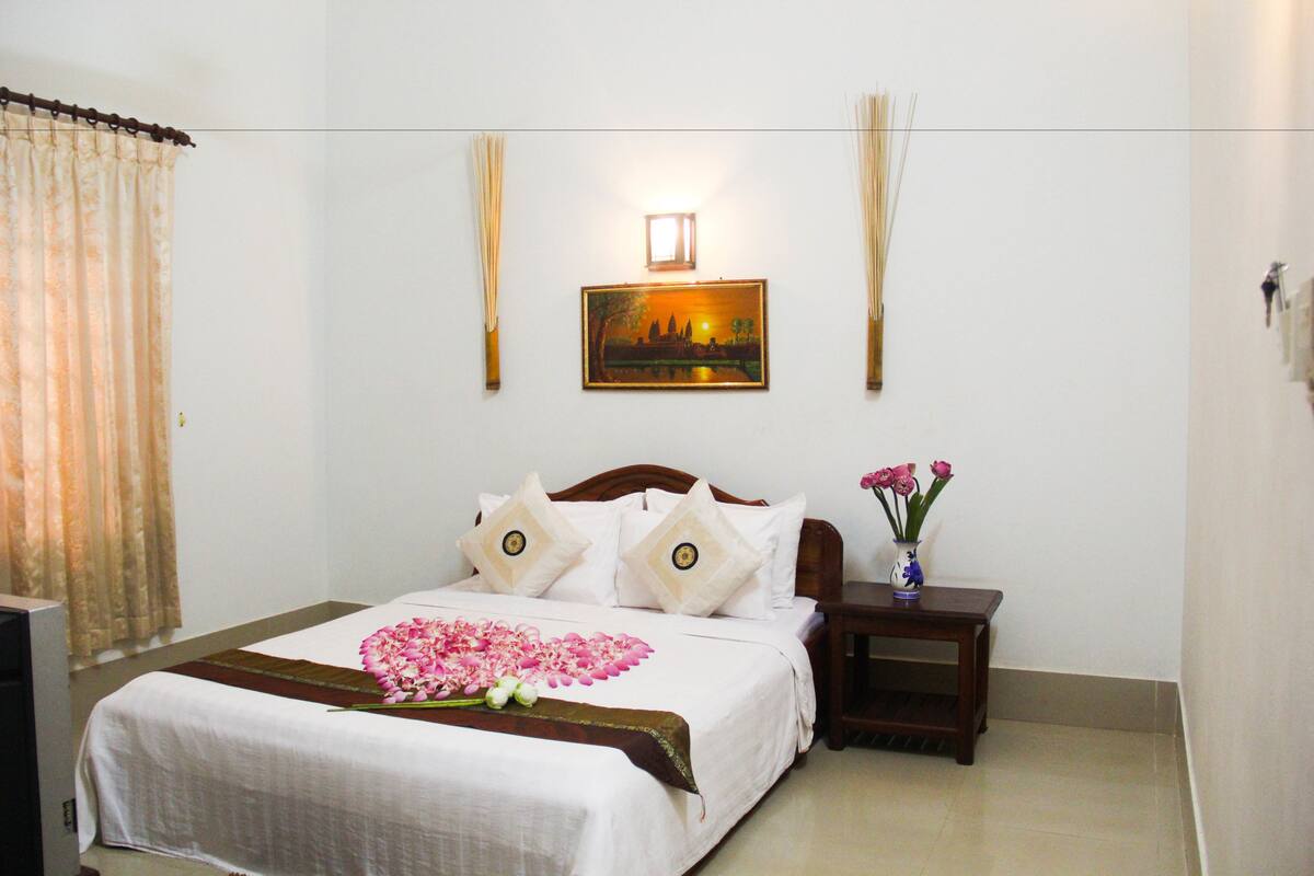 A neatly made bed with a floral arrangement, a bedside table with a vase of flowers, and a wall-mounted picture.