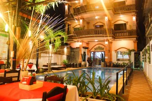 An indoor swimming pool with a poolside area, surrounded by potted plants and a dining area with a red tablecloth. - Tropical Breeze Guesthouse (Siem Reap)