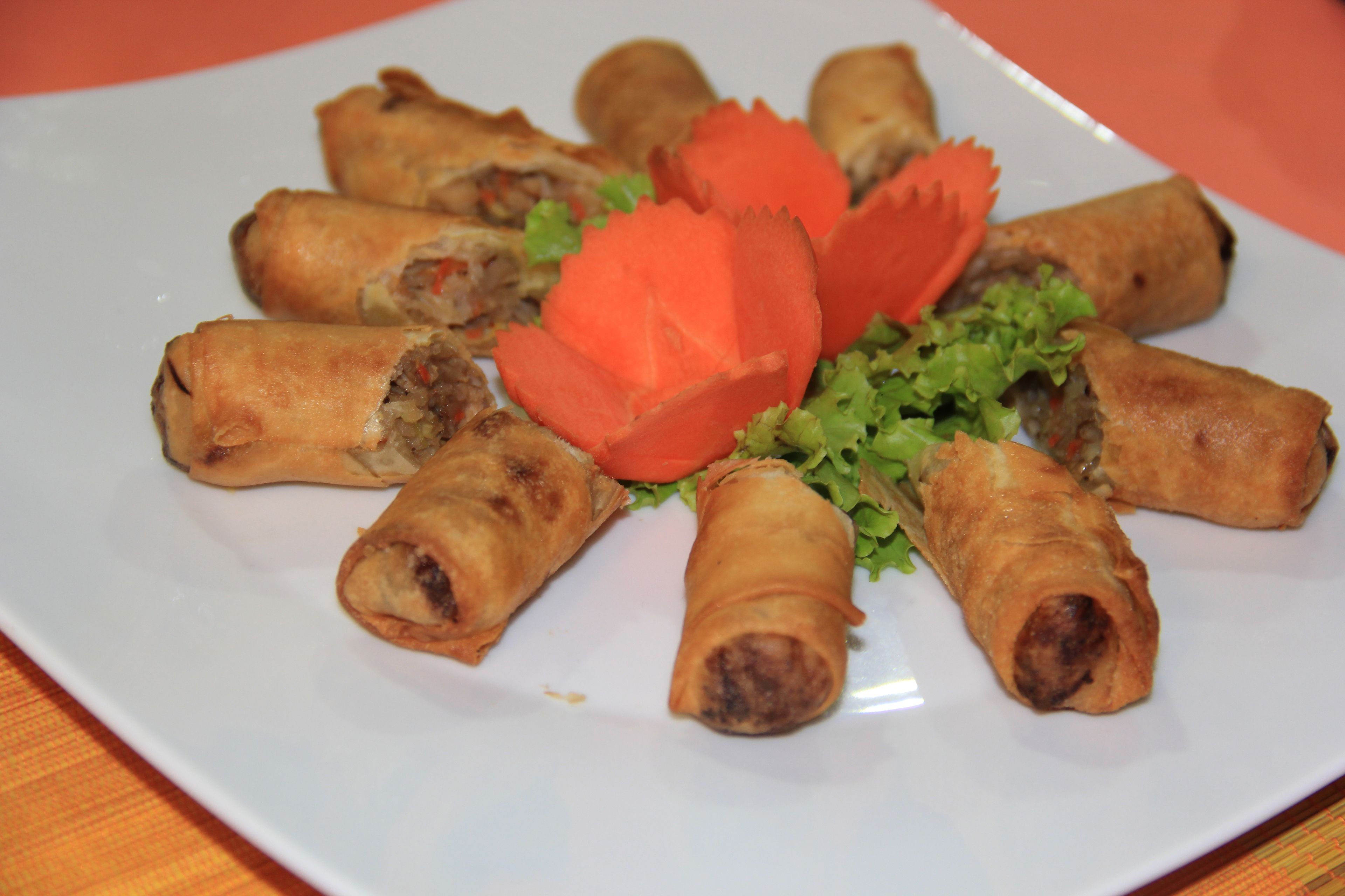 A plate of spring rolls arranged in a circular pattern with a decorative red garnish.
