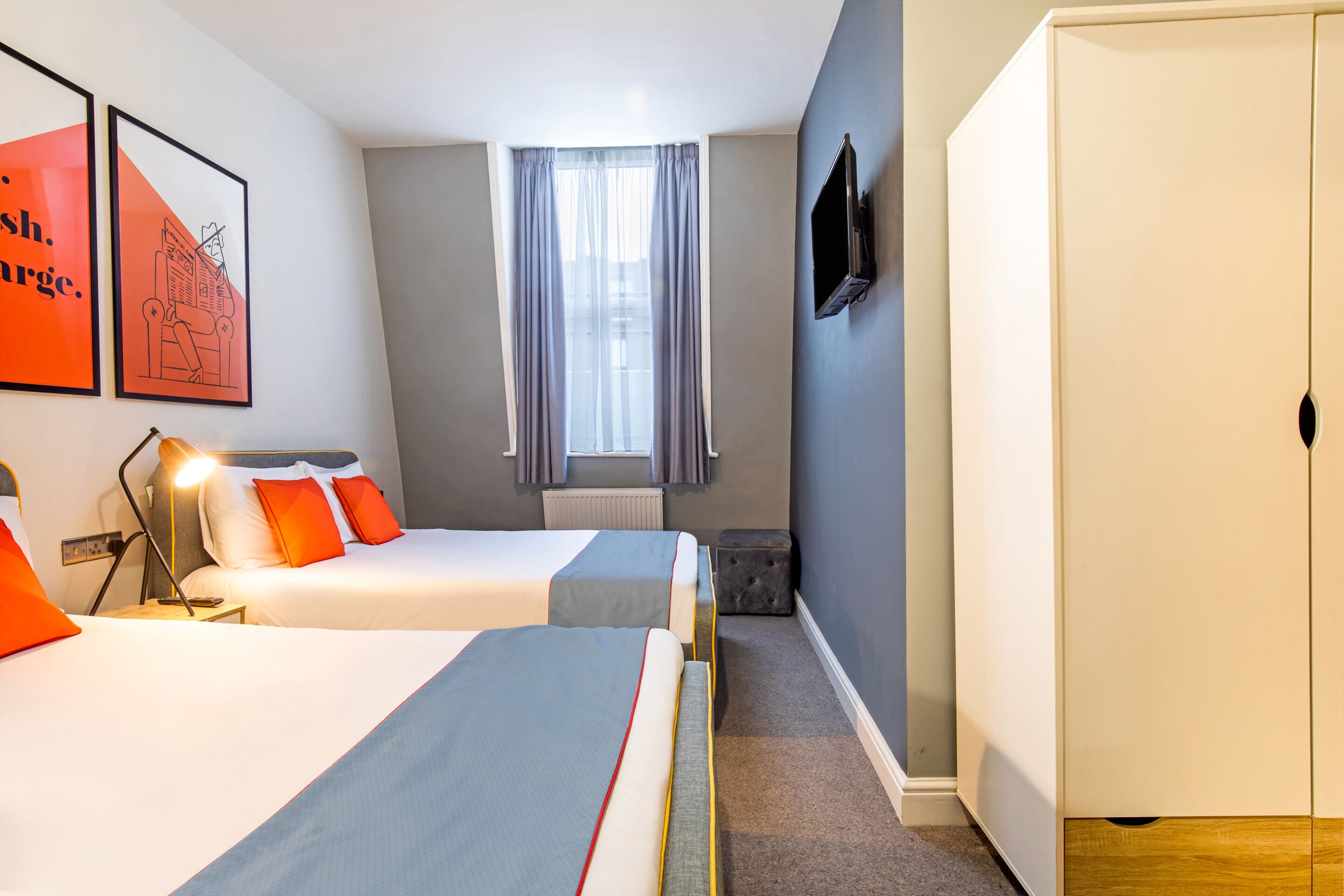 A hotel room with two beds, a wardrobe, a television, and a window with curtains.