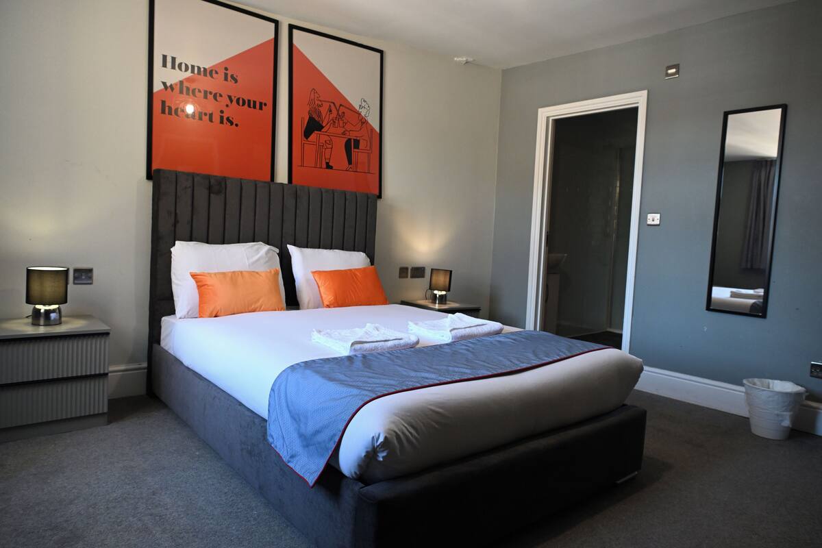 Une chambre d’hôtel bien rangée, avec un lit, deux tables de chevet, une commode, un miroir et une porte.
