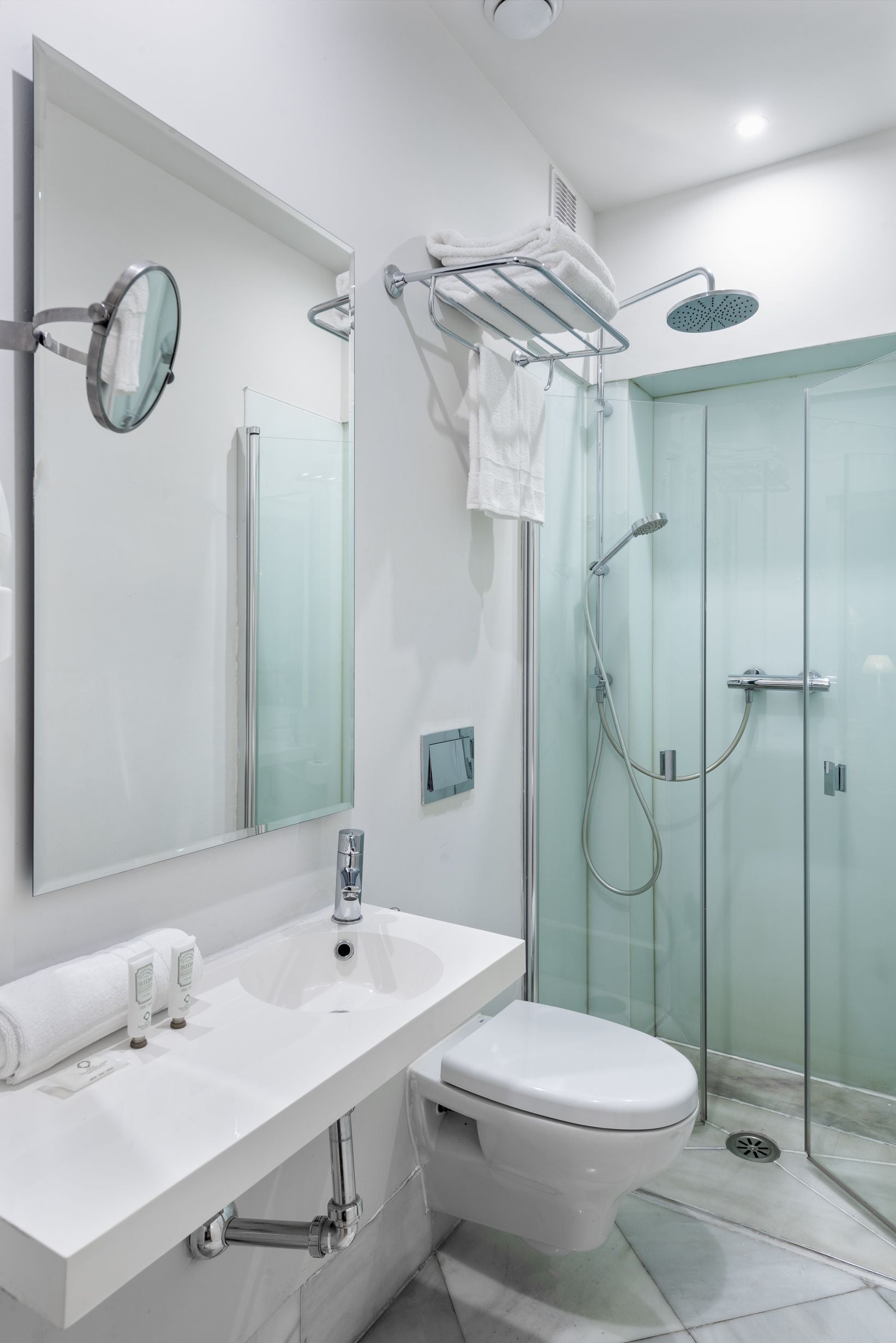 Une salle de bain moderne avec un lavabo blanc, des toilettes, une douche en verre et un grand miroir.