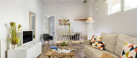 A modern living room with a sofa, coffee table, TV, and a dining area with chairs and a table.