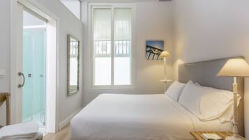 Ein Hotelzimmer mit einem Bett, einem Nachttisch mit Lampe, einem Sessel und einer Tür, die auf einen Balkon führt.