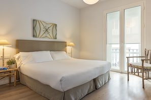 A neatly made bed with a headboard, two bedside lamps, a small table with a plant, and a chair.